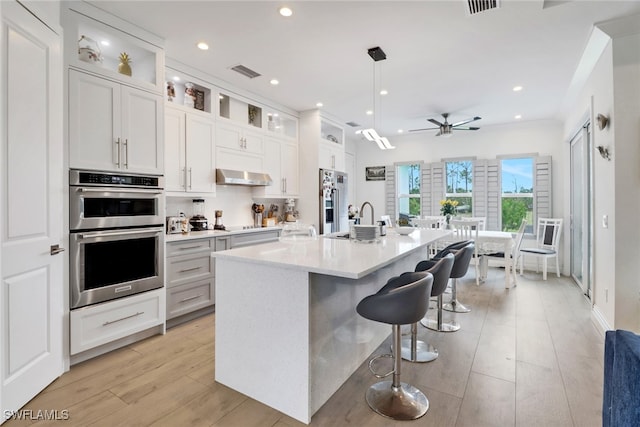 kitchen featuring a center island with sink, visible vents, range hood, stainless steel appliances, and light countertops