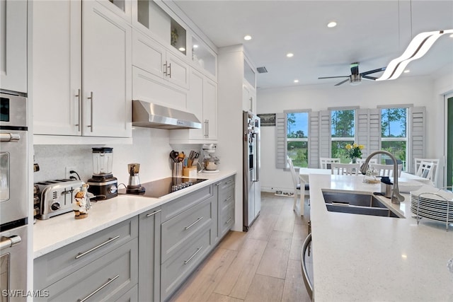 kitchen featuring a wealth of natural light, black electric stovetop, ventilation hood, and a sink