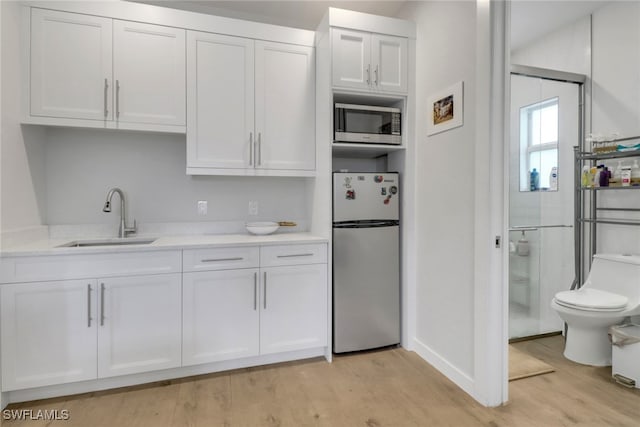 kitchen with stainless steel appliances, light countertops, a sink, and white cabinetry