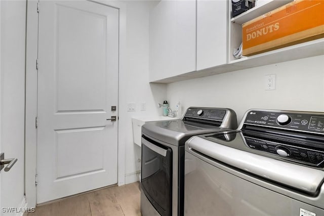 clothes washing area featuring cabinet space, washer and clothes dryer, and light wood finished floors