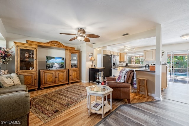 living room with ceiling fan, light wood finished floors, visible vents, and baseboards