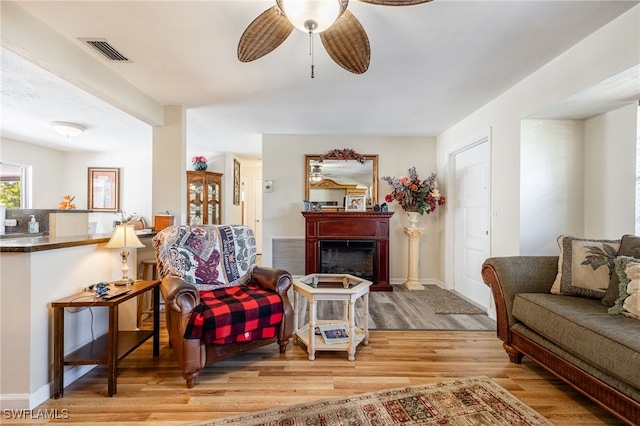 interior space with a fireplace, visible vents, a ceiling fan, wood finished floors, and baseboards