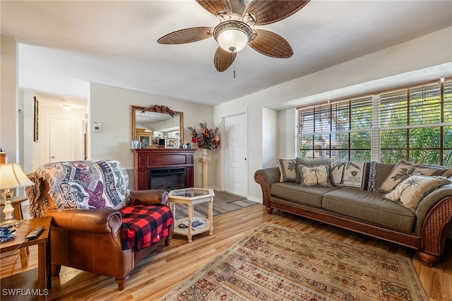 living area with a glass covered fireplace, wood finished floors, and a ceiling fan