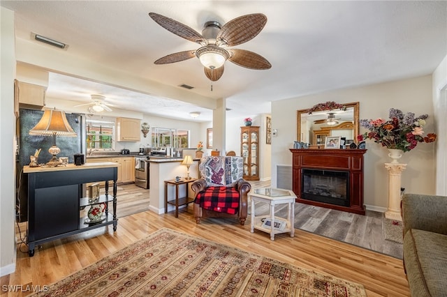 living room with light wood-style floors, baseboards, visible vents, and a glass covered fireplace