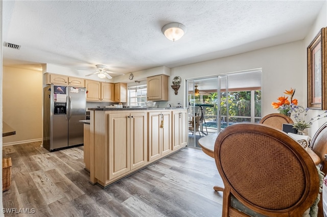 kitchen with light wood-type flooring, stainless steel refrigerator with ice dispenser, light brown cabinets, and a healthy amount of sunlight