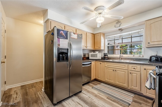 kitchen featuring dark countertops, stainless steel appliances, light wood-style floors, light brown cabinets, and a sink