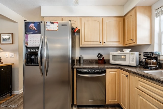 kitchen featuring dark countertops, light brown cabinetry, white microwave, wood finished floors, and stainless steel fridge with ice dispenser