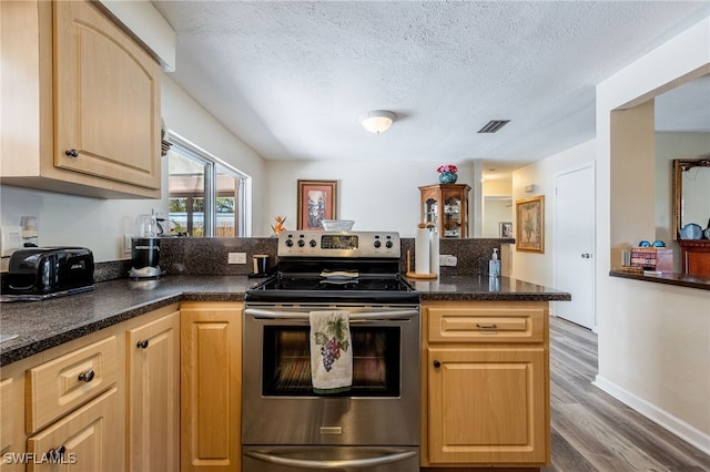 kitchen featuring a textured ceiling, a peninsula, wood finished floors, visible vents, and electric stove