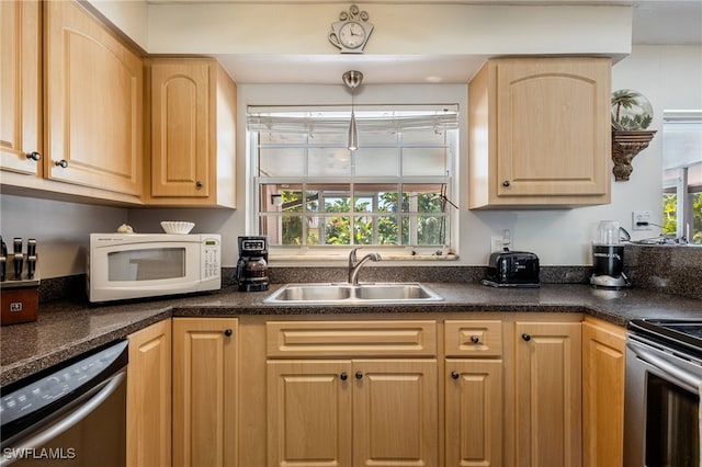 kitchen featuring light brown cabinets, stainless steel appliances, dark countertops, and a sink