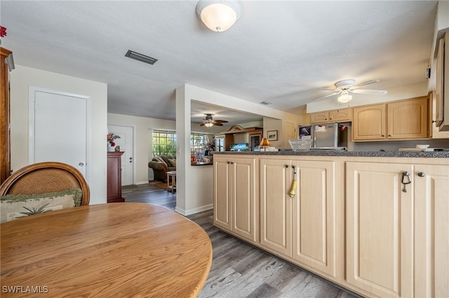 kitchen with dark countertops, ceiling fan, stainless steel refrigerator, wood finished floors, and a peninsula