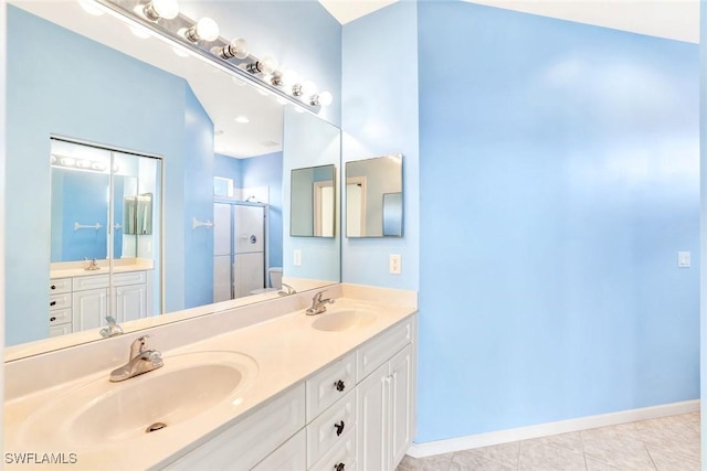 bathroom with double vanity, a shower stall, baseboards, and a sink