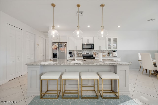 kitchen with appliances with stainless steel finishes, a kitchen island with sink, white cabinetry, light tile patterned floors, and a sink