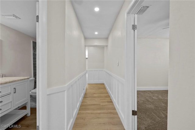 hallway featuring recessed lighting, a wainscoted wall, a decorative wall, visible vents, and light wood finished floors