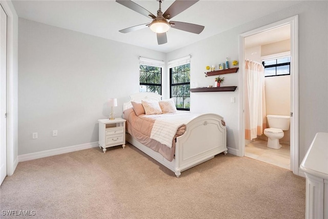 bedroom with baseboards, light colored carpet, ceiling fan, and ensuite bath