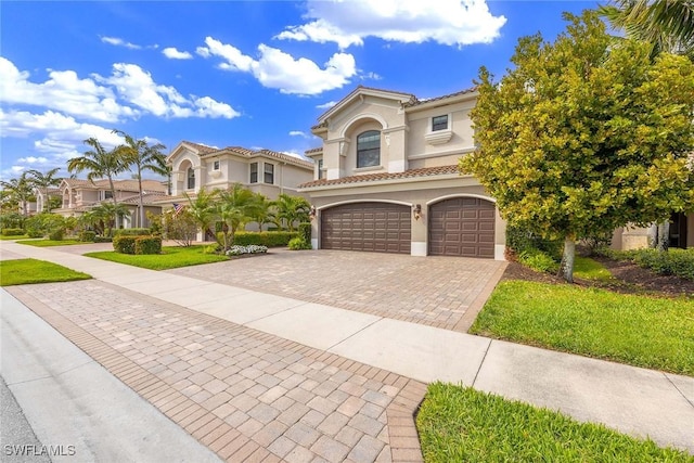 mediterranean / spanish house with decorative driveway, a tiled roof, an attached garage, and stucco siding