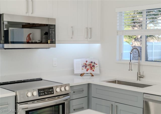 kitchen featuring stainless steel appliances, gray cabinets, light countertops, and a sink