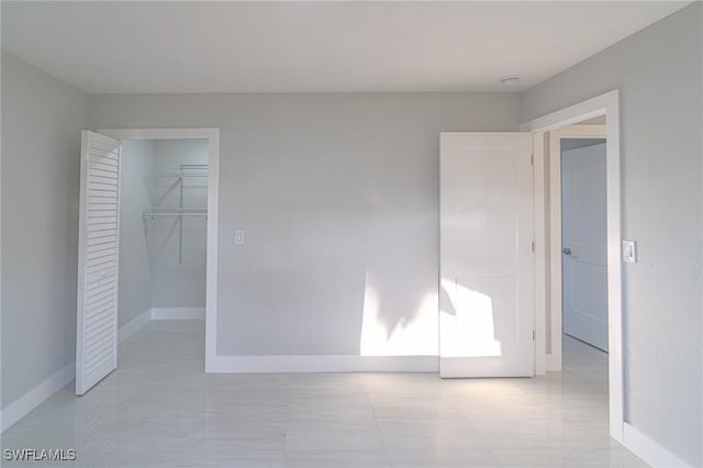 unfurnished bedroom with a walk in closet, a closet, and baseboards