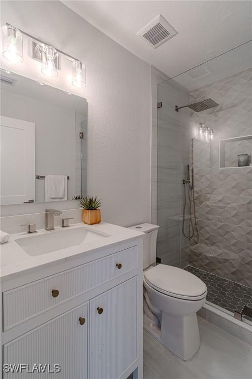 bathroom with toilet, vanity, walk in shower, and visible vents