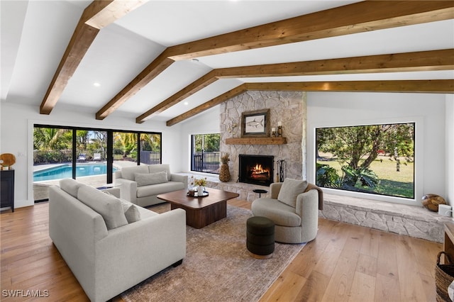 living area featuring a stone fireplace, lofted ceiling with beams, and wood-type flooring