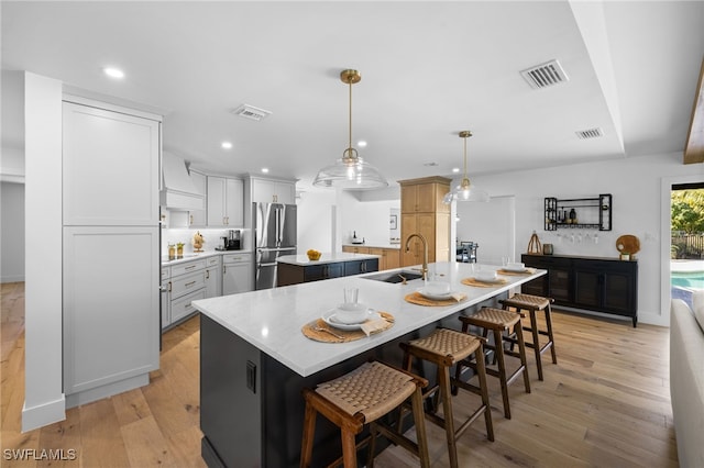 kitchen featuring freestanding refrigerator, visible vents, an island with sink, and a sink