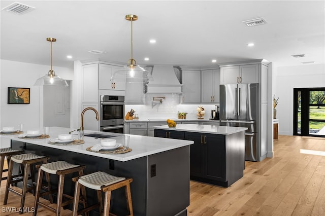 kitchen with a kitchen island with sink, visible vents, premium range hood, stainless steel appliances, and a sink