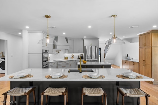 kitchen featuring premium range hood, a sink, a spacious island, stainless steel appliances, and washer / dryer