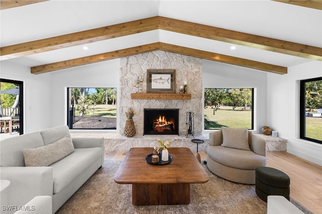 living room with a stone fireplace, vaulted ceiling with beams, wood finished floors, and plenty of natural light