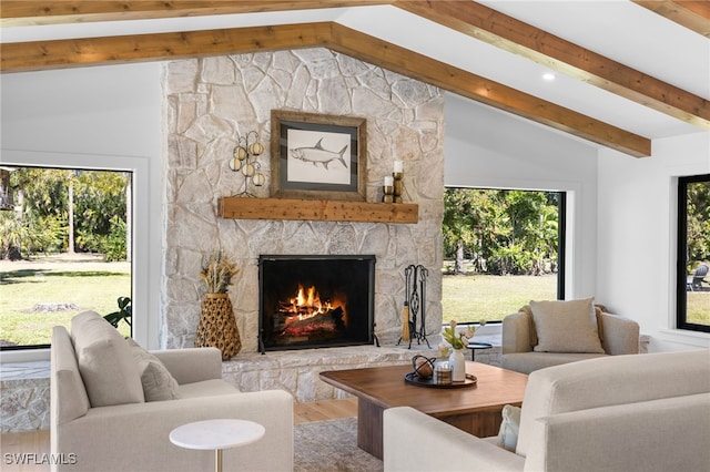 living area with a stone fireplace, a healthy amount of sunlight, vaulted ceiling with beams, and wood finished floors