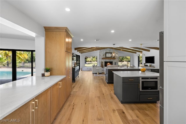 kitchen with vaulted ceiling with beams, open floor plan, light wood-type flooring, light countertops, and stainless steel oven