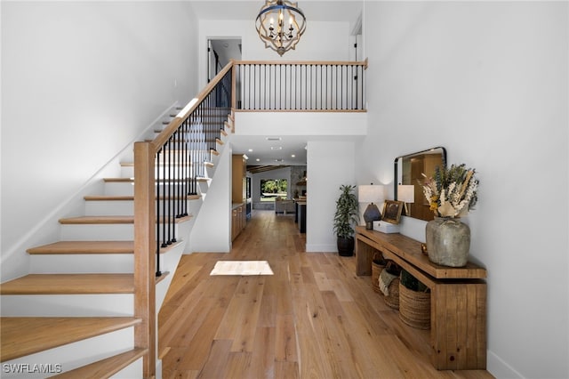 entryway with stairway, wood-type flooring, a high ceiling, and a chandelier