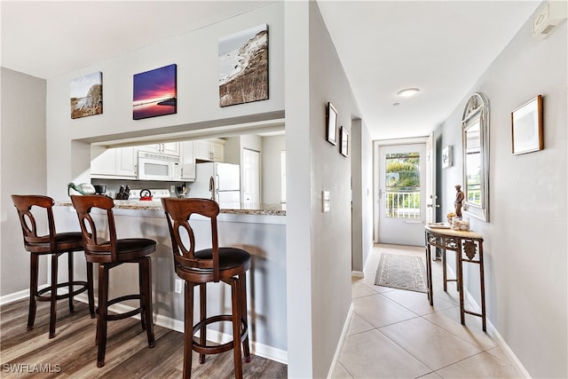 kitchen featuring a breakfast bar area, white cabinetry, white appliances, a peninsula, and baseboards