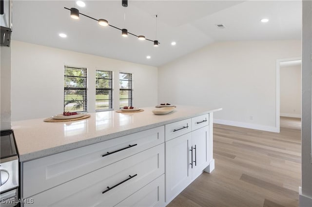 kitchen featuring light wood finished floors, baseboards, lofted ceiling, light stone countertops, and white cabinetry