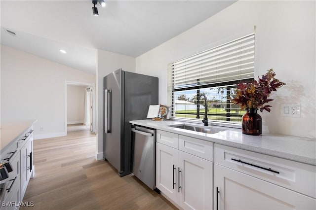 kitchen with white cabinets, light stone counters, stainless steel appliances, light wood-type flooring, and a sink