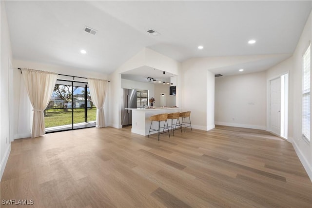 unfurnished living room with light wood-type flooring, baseboards, visible vents, and vaulted ceiling