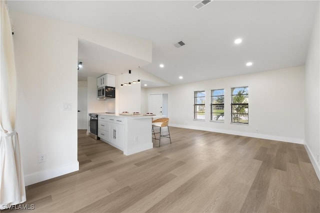 kitchen with white cabinetry, vaulted ceiling, stainless steel microwave, and a kitchen breakfast bar