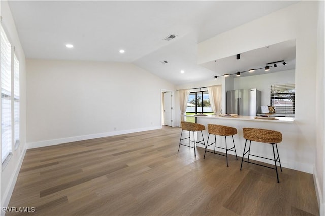 kitchen featuring lofted ceiling, visible vents, a kitchen breakfast bar, freestanding refrigerator, and light wood finished floors