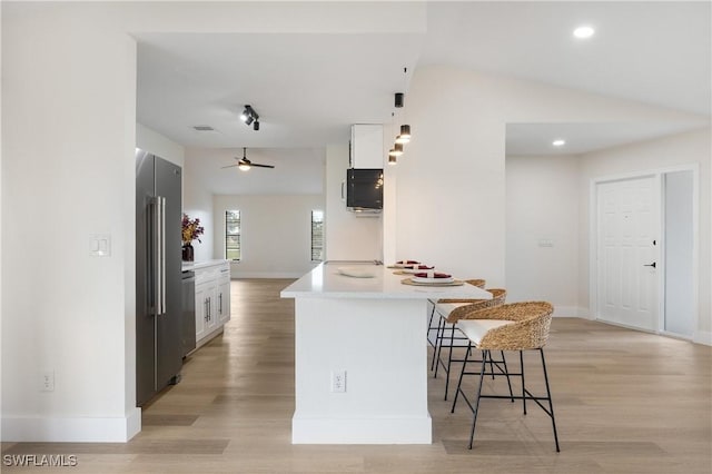 kitchen featuring lofted ceiling, high end refrigerator, a kitchen bar, and white cabinets