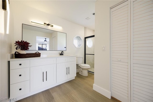 full bath with toilet, ceiling fan, wood finished floors, walk in shower, and vanity