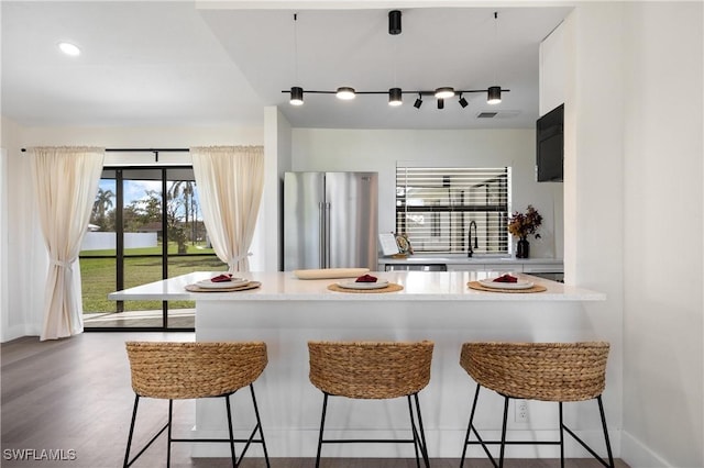 kitchen with light countertops, a breakfast bar, a sink, and freestanding refrigerator