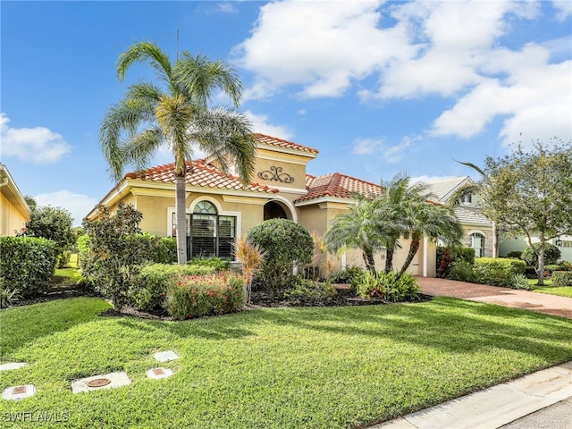 mediterranean / spanish home with a front lawn, an attached garage, a tile roof, and stucco siding