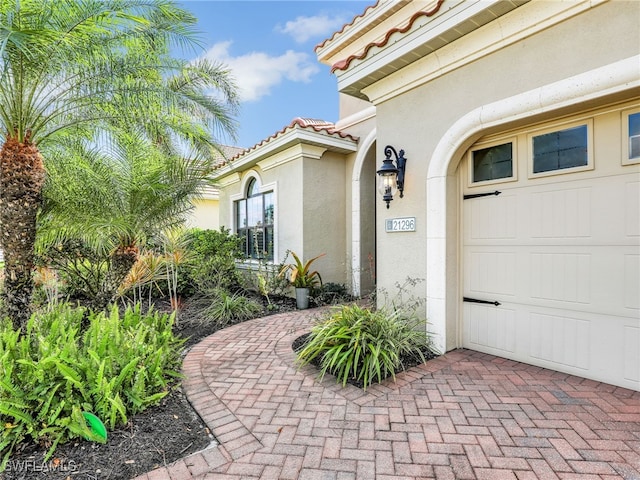 doorway to property with an attached garage, a tile roof, and stucco siding