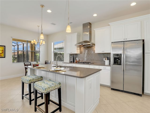 kitchen with tasteful backsplash, stainless steel appliances, wall chimney range hood, a sink, and light tile patterned flooring