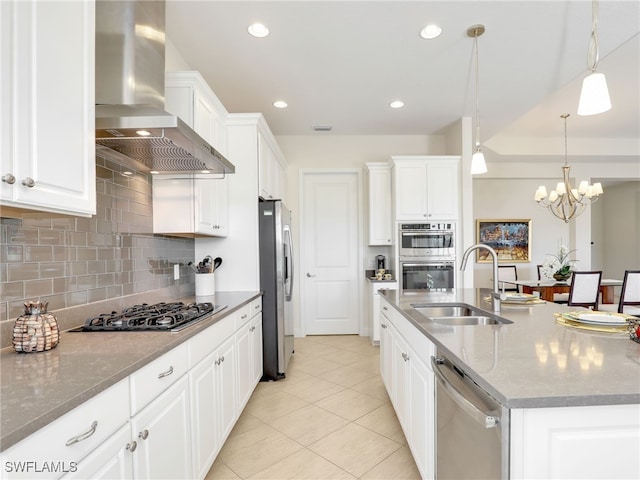 kitchen with decorative backsplash, appliances with stainless steel finishes, wall chimney range hood, white cabinetry, and a sink