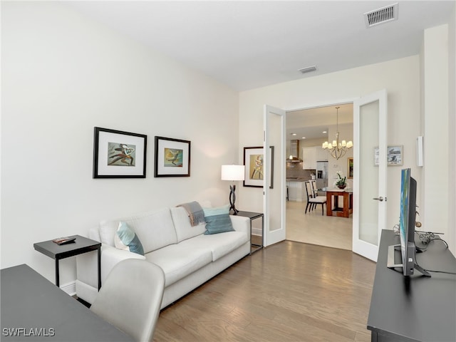 living area featuring a chandelier, french doors, visible vents, and wood finished floors