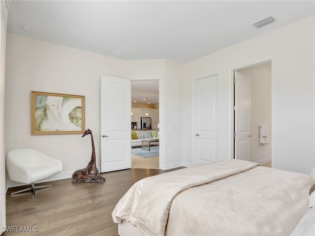 bedroom featuring stainless steel fridge, baseboards, visible vents, connected bathroom, and wood finished floors