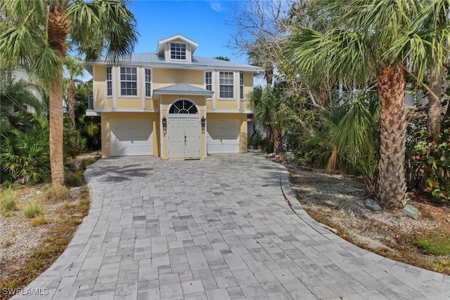 raised beach house with decorative driveway, an attached garage, and stucco siding