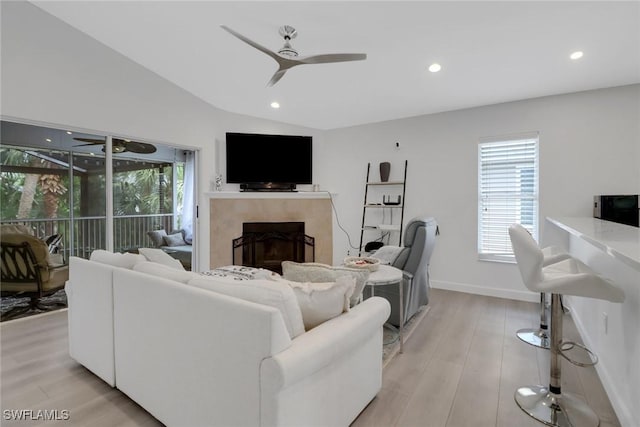 living room featuring light wood-type flooring, a fireplace, vaulted ceiling, and ceiling fan