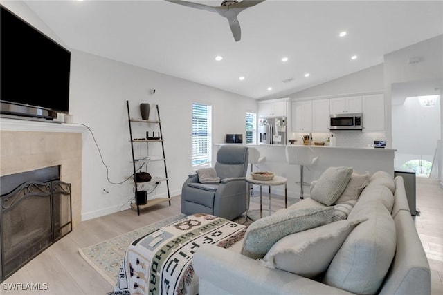 living area featuring lofted ceiling, recessed lighting, light wood-style flooring, ceiling fan, and a tile fireplace