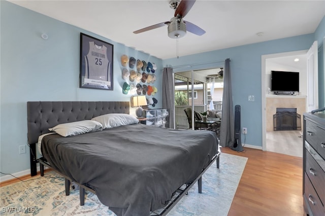 bedroom featuring a tile fireplace, baseboards, ceiling fan, and light wood finished floors