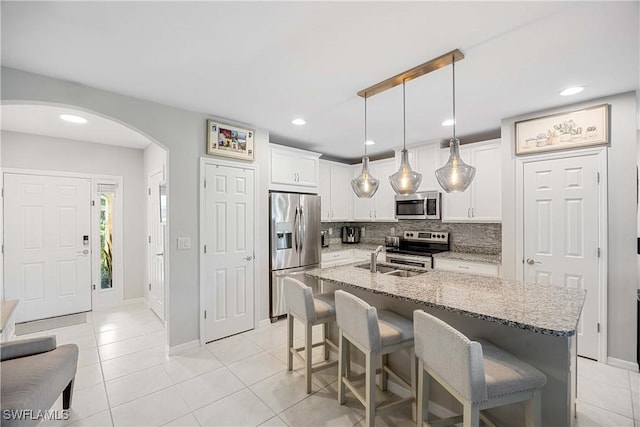 kitchen featuring a sink, tasteful backsplash, arched walkways, appliances with stainless steel finishes, and white cabinets